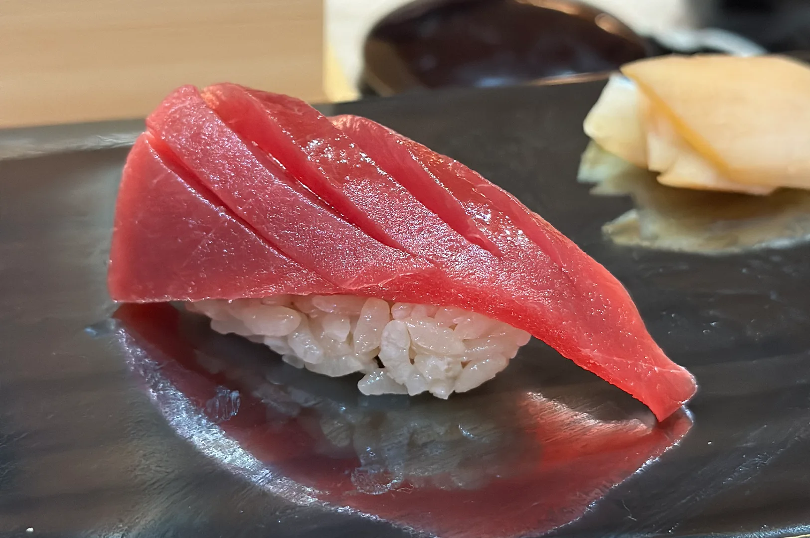 A close-up of a fresh Bluefin tuna Akami (lean tuna) nigiri sushi with precise cross-cut scoring on a black lacquer plate.