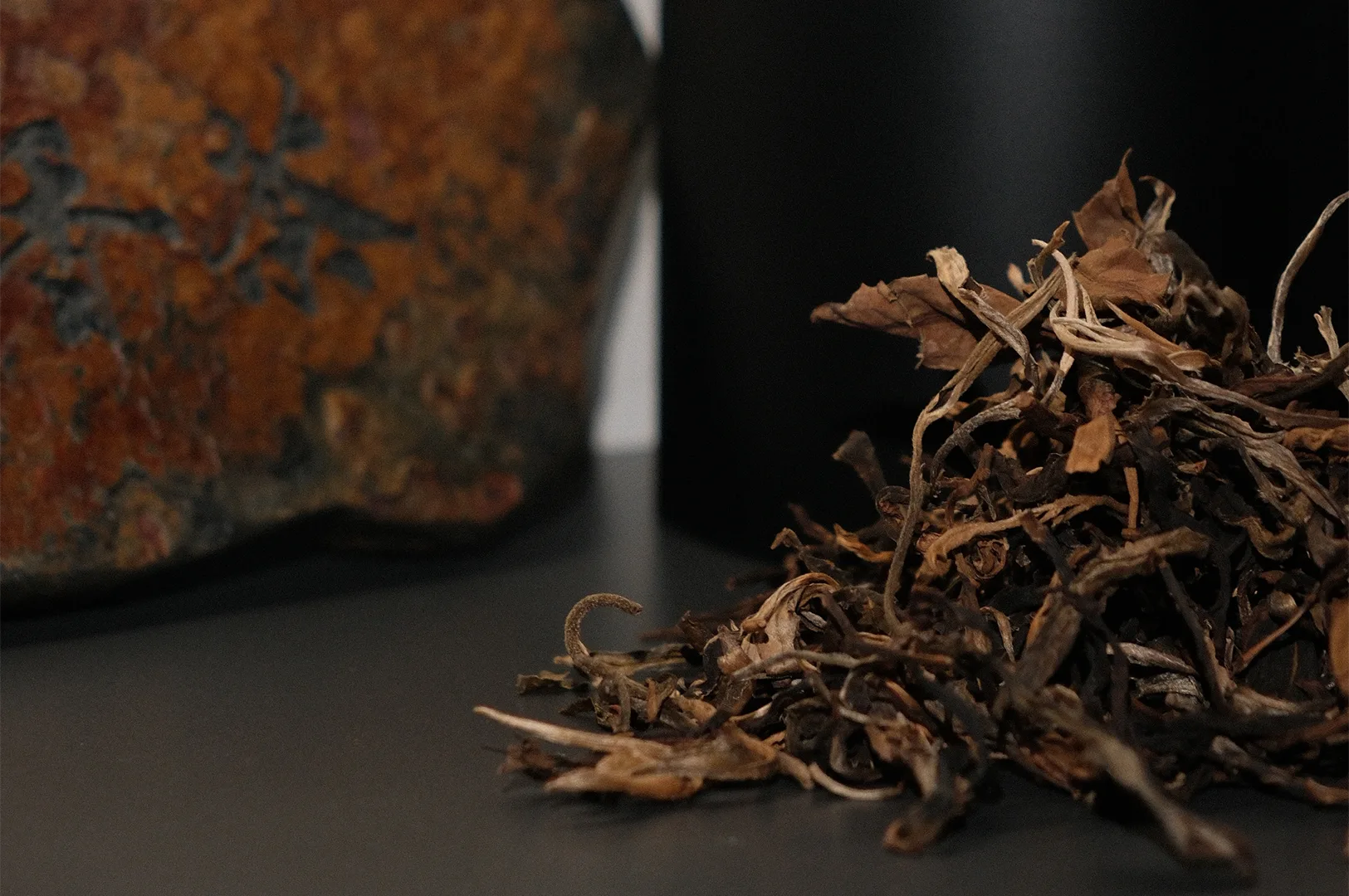 Close-up of a pile of high-quality, whole leaf dried tea showing rich textures and dark colors next to a decorative stone.