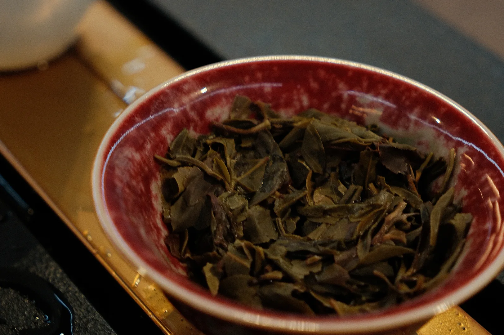 High-quality steeped whole oolong tea leaves resting in a crimson and white glazed ceramic bowl after brewing.