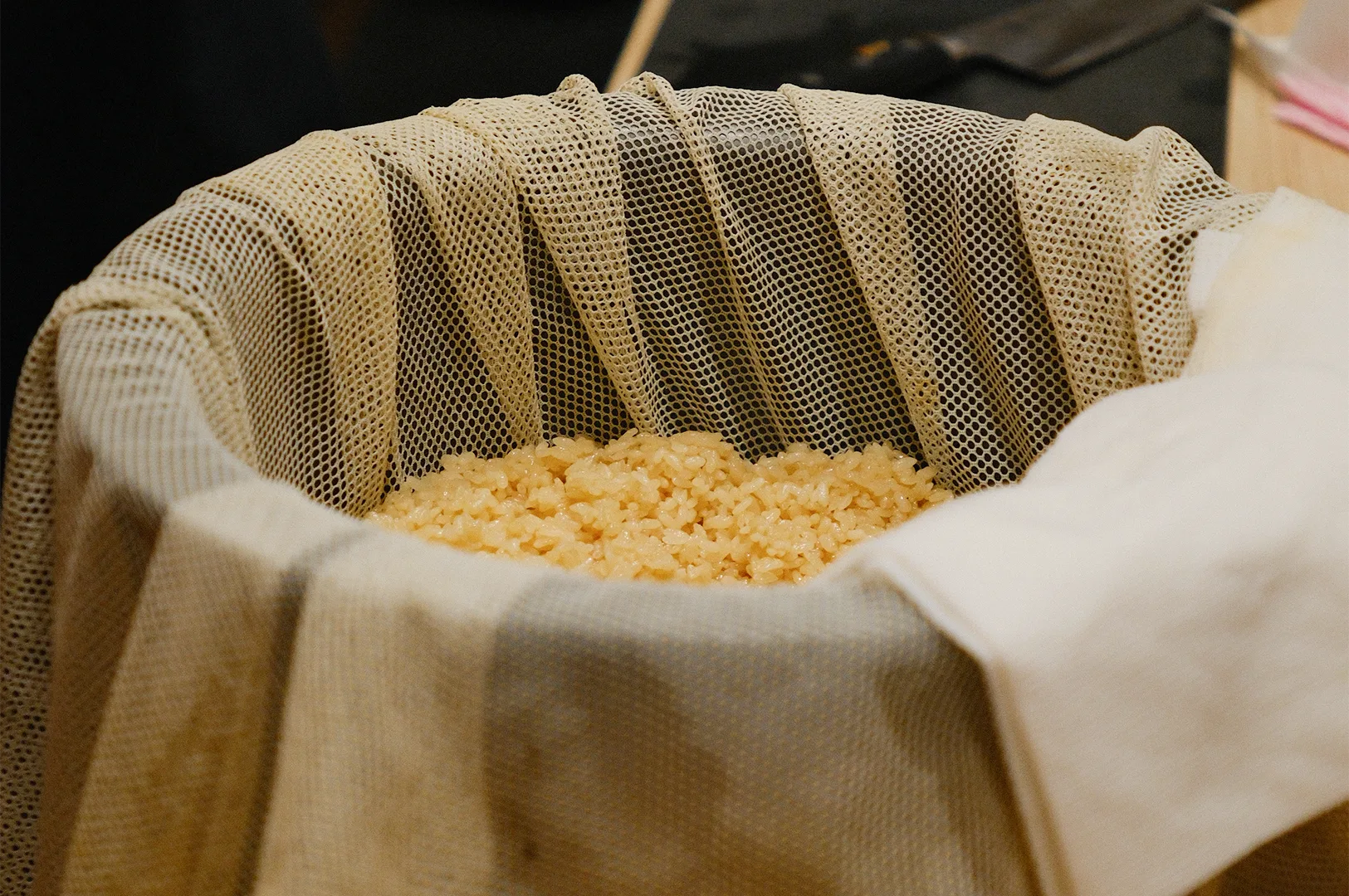 Traditional Japanese sushi rice (shari) seasoned with red vinegar resting in a wooden tub lined with a mesh cloth.