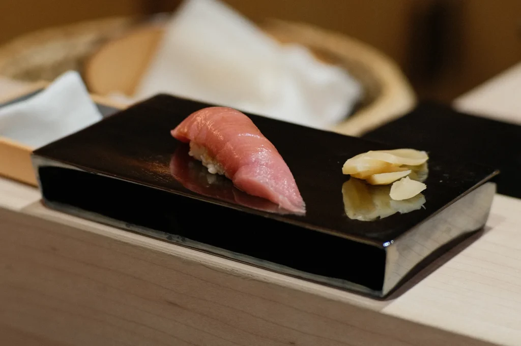 A single piece of premium fatty tuna (Otoro) nigiri sushi served on a traditional black lacquer block with pickled ginger.