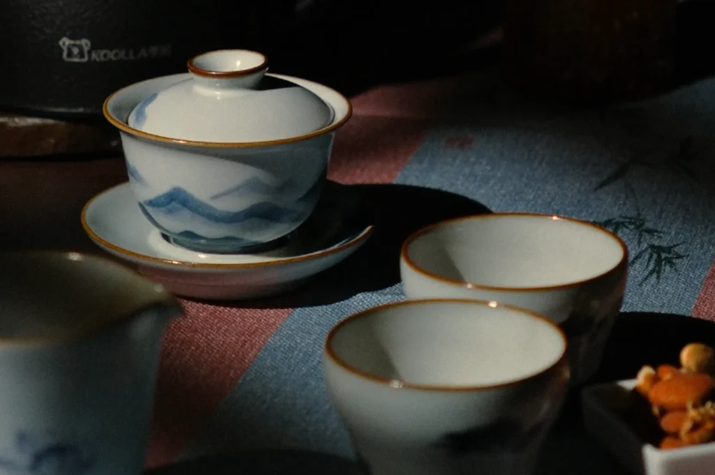 Elegant Chinese tea set with blue mountain patterns and gold rims on a dark tablecloth, bathed in soft, moody lighting.
