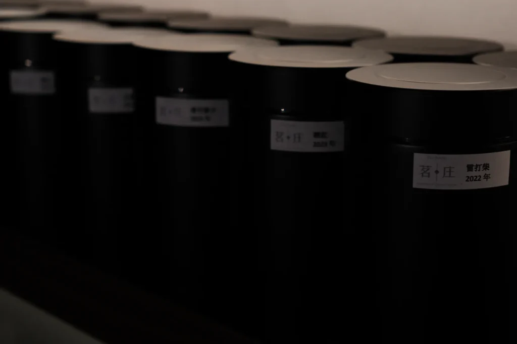 Row of black canisters with white lids, labeled in Chinese, sit on a shelf. The labels have a minimalist design, conveying a calm, organized atmosphere.