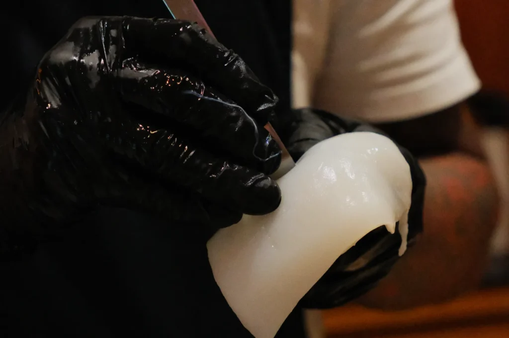 Gloved hands mold a glossy, translucent white substance, possibly wax or clay. The focus is on craftsmanship and precision, suggesting creativity.