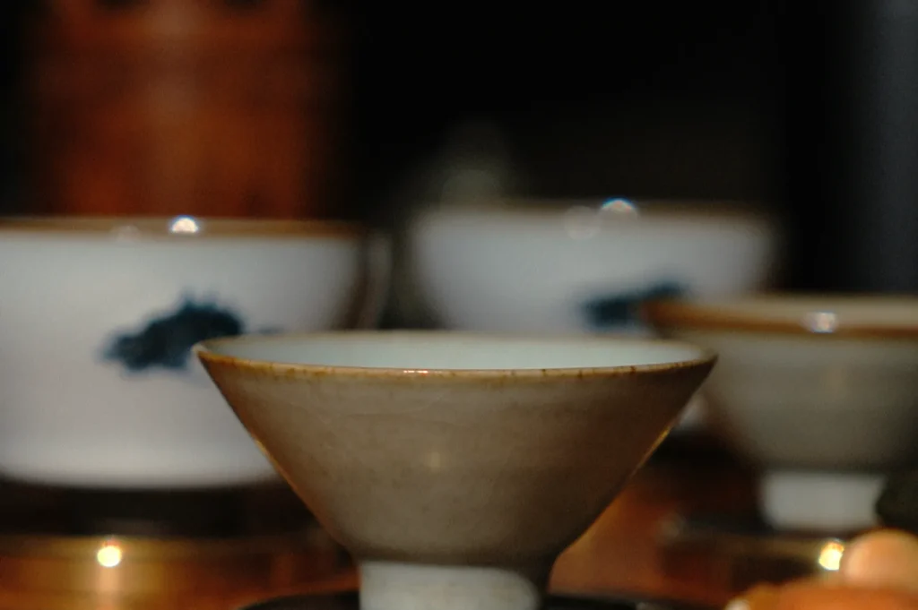 Close-up of a rustic, ceramic teacup on a wooden surface, surrounded by blurred similar cups with a dark background, conveying a calm, cozy atmosphere.