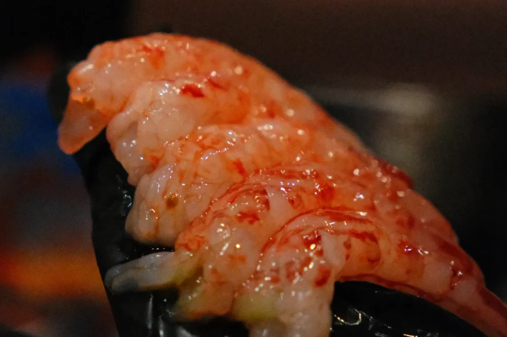Close-up of raw prawns on a black plate, with a glossy texture and light reflections. The image conveys freshness and a rich, appetizing tone.