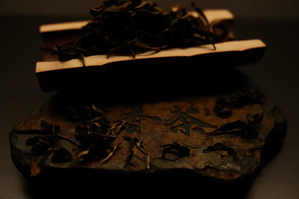 Dark, rustic carved stone with Chinese characters showcases dried tea leaves, creating an earthy, traditional feel. Warm tones and soft lighting.