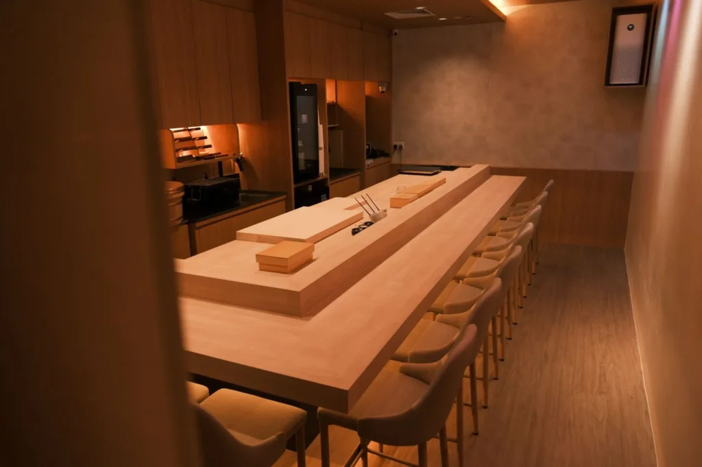 Minimalist sushi bar with a light wood counter, surrounded by beige chairs. The warm lighting creates an inviting, intimate ambiance.