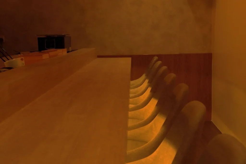 Warmly lit, minimalist bar setting with empty, curved chairs in a row beside a long wooden counter. A calming, cozy ambiance prevails.