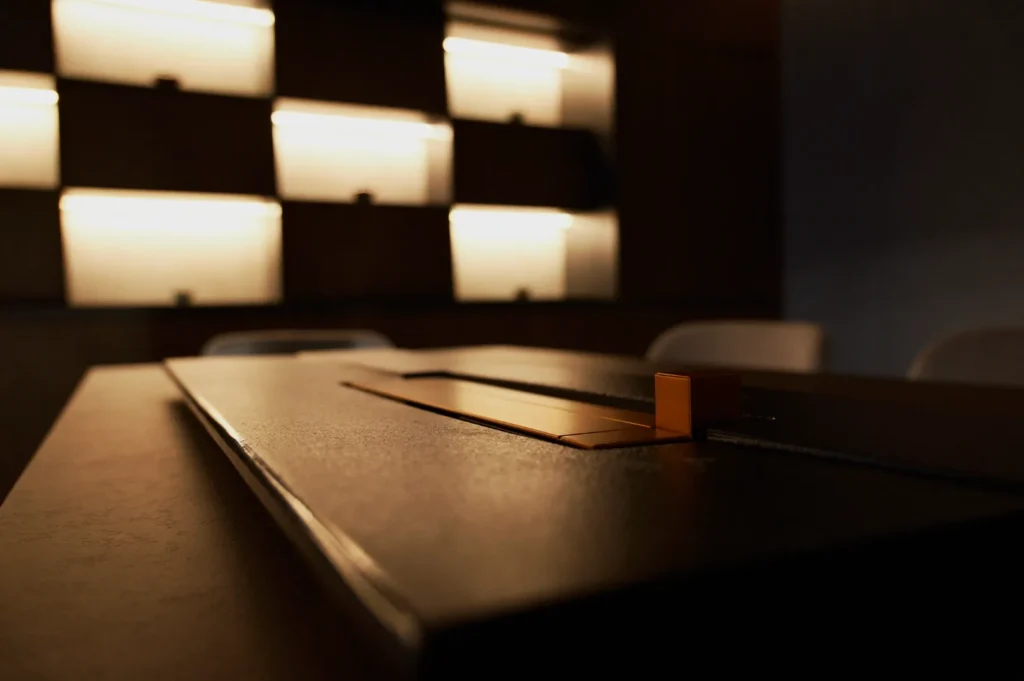 Dim, cozy room with a modern design. Soft lighting illuminates horizontal paneling on the wall, creating a warm and inviting ambiance. A sleek table in the foreground.