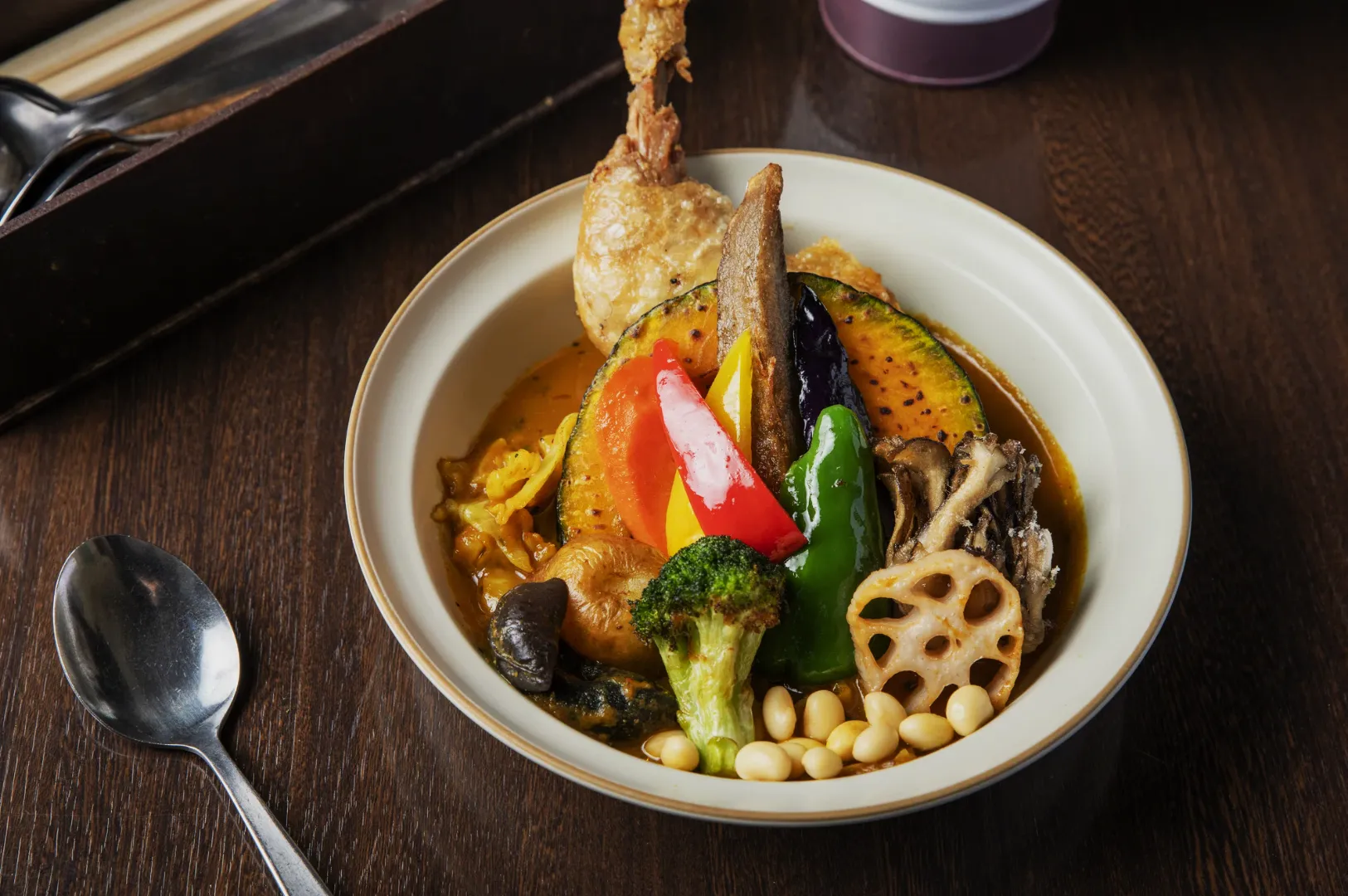 A bowl of vibrant Japanese curry soup with chicken, broccoli, peppers, lotus root, eggplant, and soybeans, exuding a savory and colorful appeal.