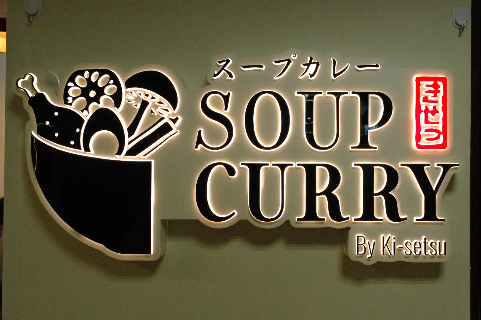 Sign for a soup curry restaurant featuring the text "SOUP CURRY" and a graphic of a bowl with various ingredients.