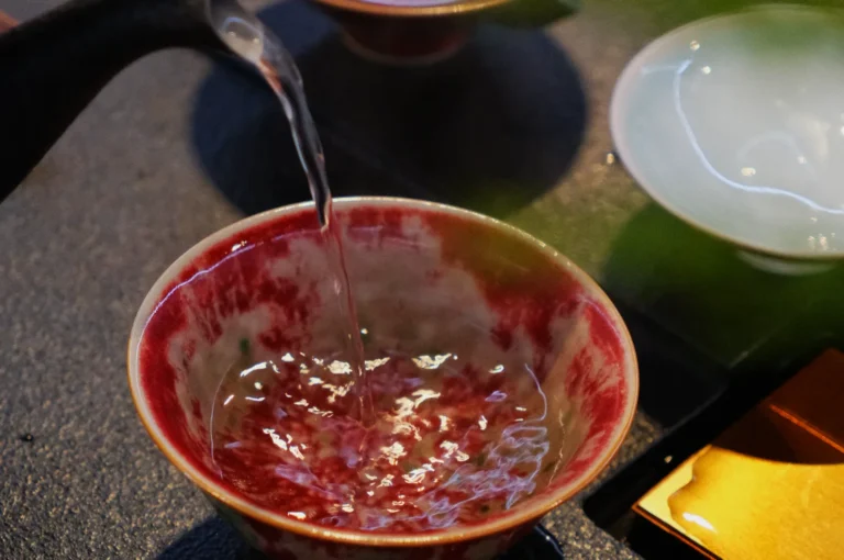 A delicate stream of water pours into a vibrant red and white ceramic bowl on a table, evoking a calm and reflective mood in the setting.