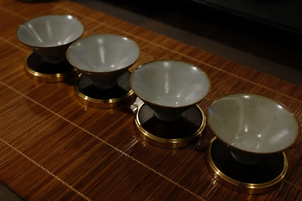 Four white ceramic bowls with gold rims, placed on a bamboo mat in a row. The setting conveys an elegant and serene atmosphere.