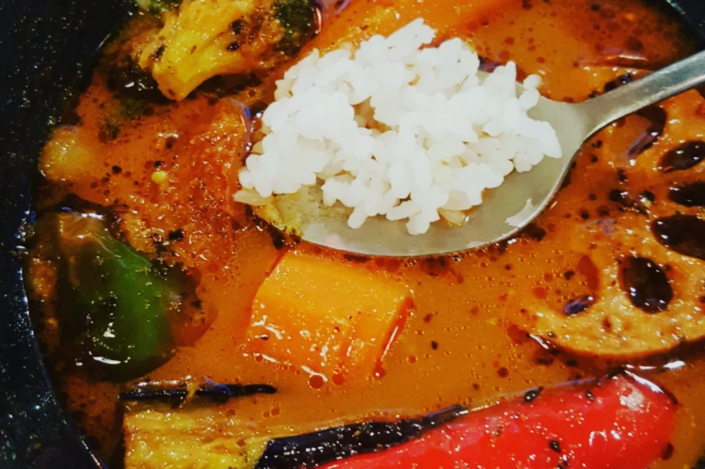 A colorful bowl of vegetable curry with rice. Features red and green peppers, lotus root, and broccoli, creating a vibrant and hearty meal.