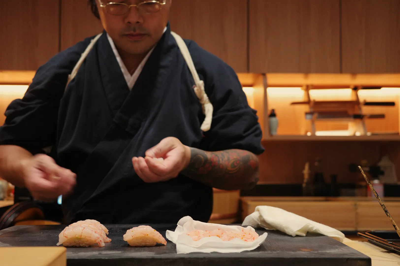 Chef Masa in traditional attire preparing sushi at a restaurant.