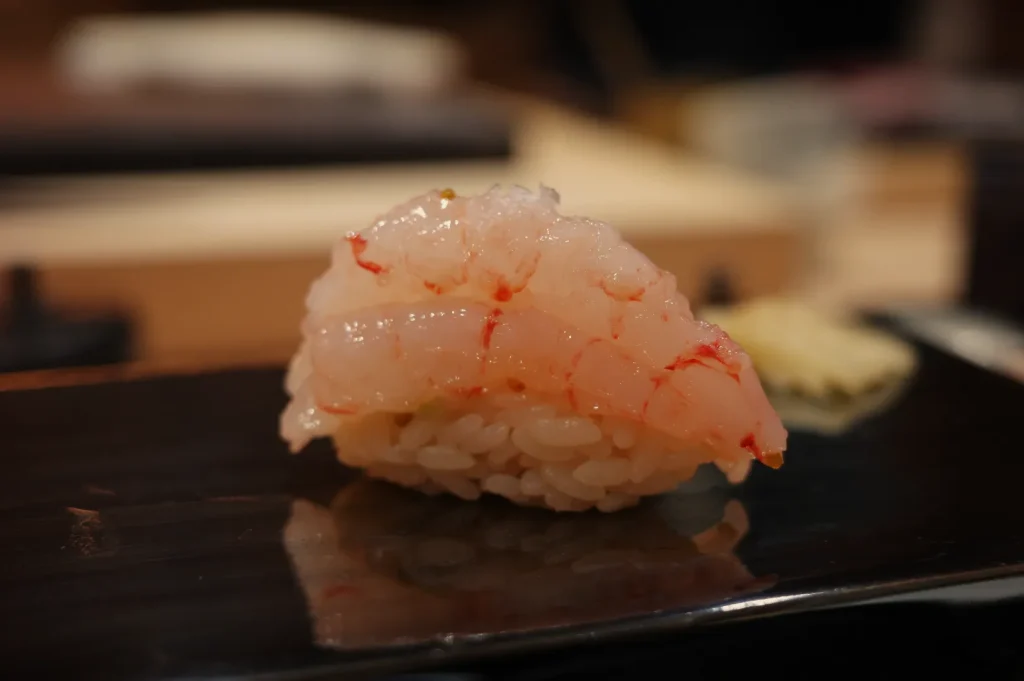 A piece of sushi with shrimp on a black plate, accompanied by a small serving of wasabi.