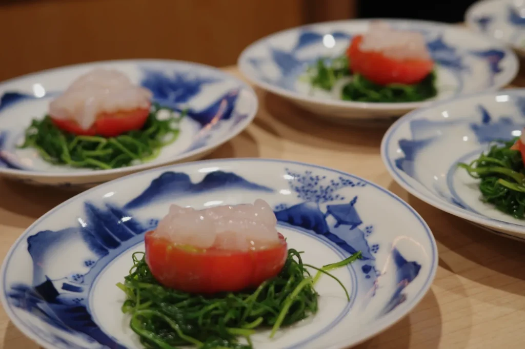 Plates with a dish consisting of a tomato filled with seafood, served on a bed of seaweed.