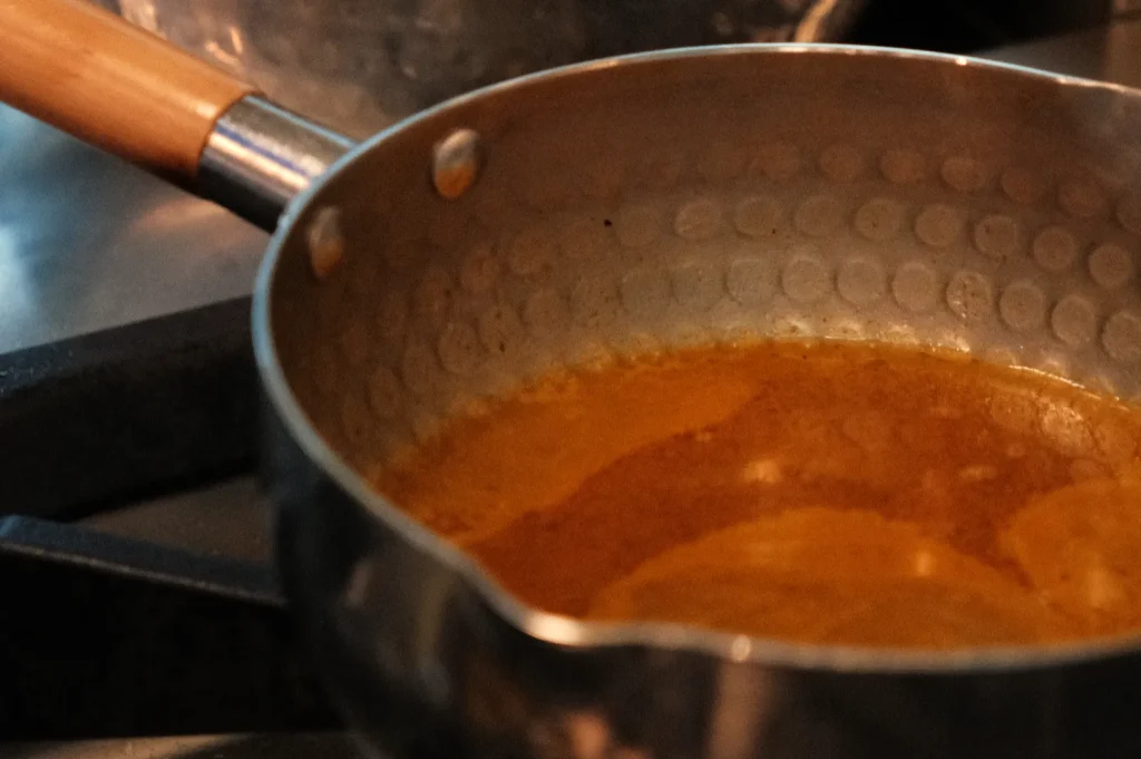 A close-up of a metal saucepan with golden liquid inside, sitting on a stove.