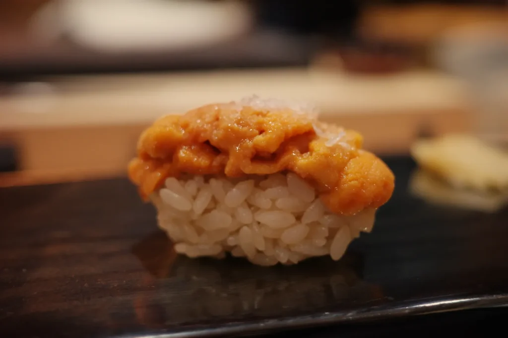 A piece of sushi featuring a mound of sea urchin (uni) atop a small serving of rice.