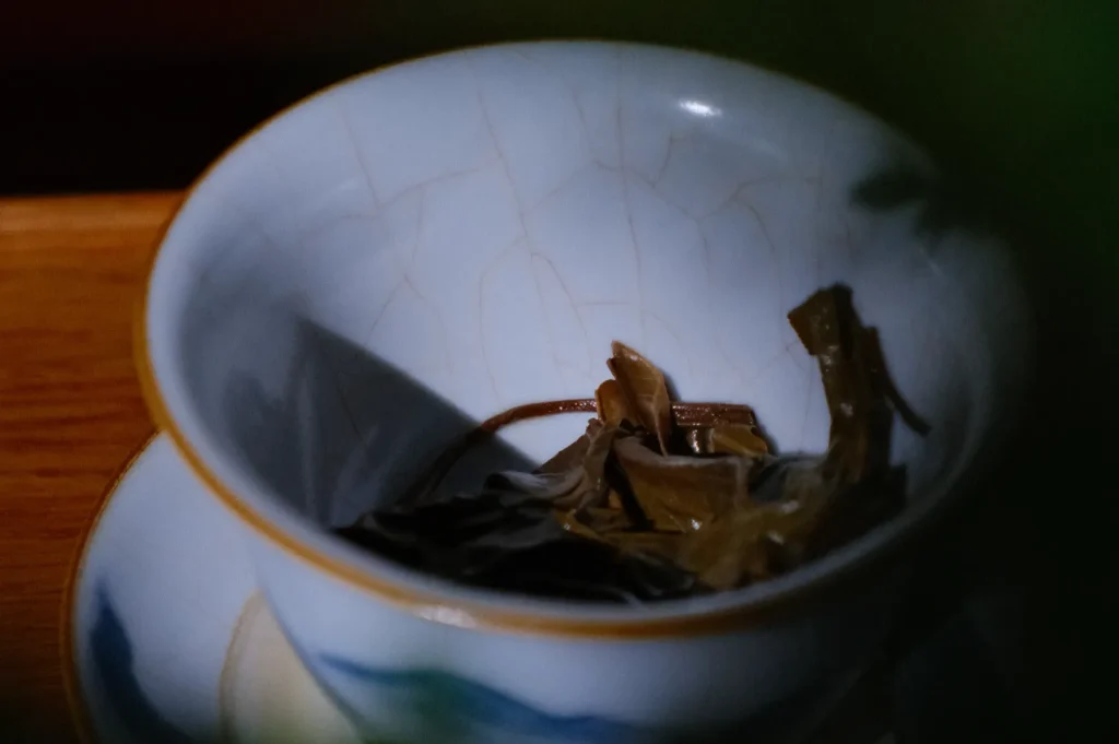 A close-up of a cup containing dried tea leaves, with soft lighting casting shadows on the surface.