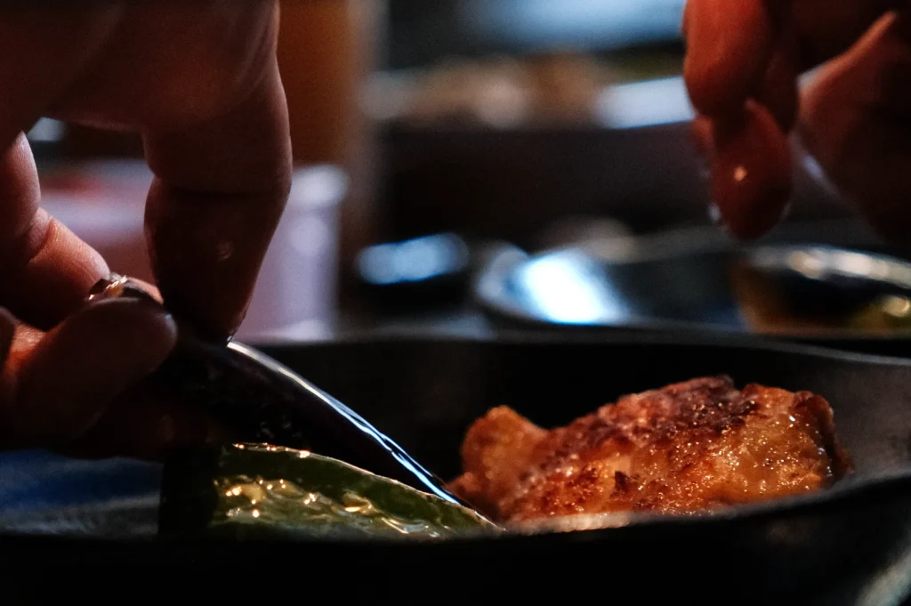 A close-up of hands using a fork to pick up a piece of food from a plate.