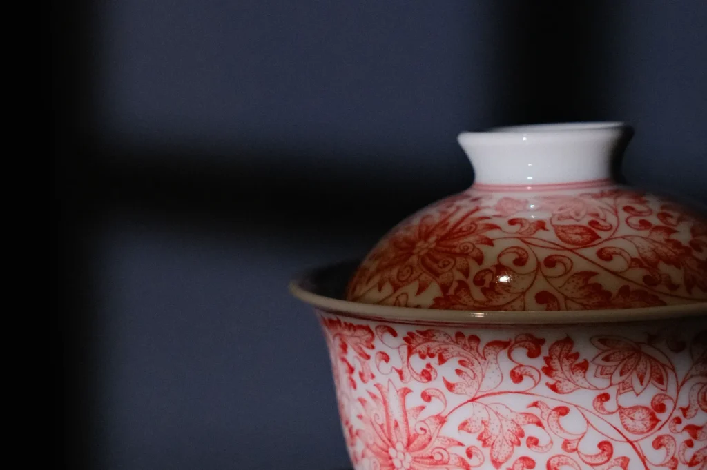 A decorative porcelain bowl with a lid, featuring a red floral pattern against a dark background.