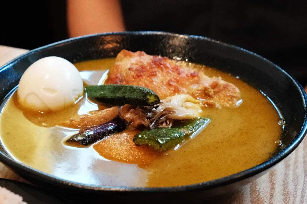 A bowl of soup curry with a variety of ingredients including a soft boiled egg, chicken, and vegetables.