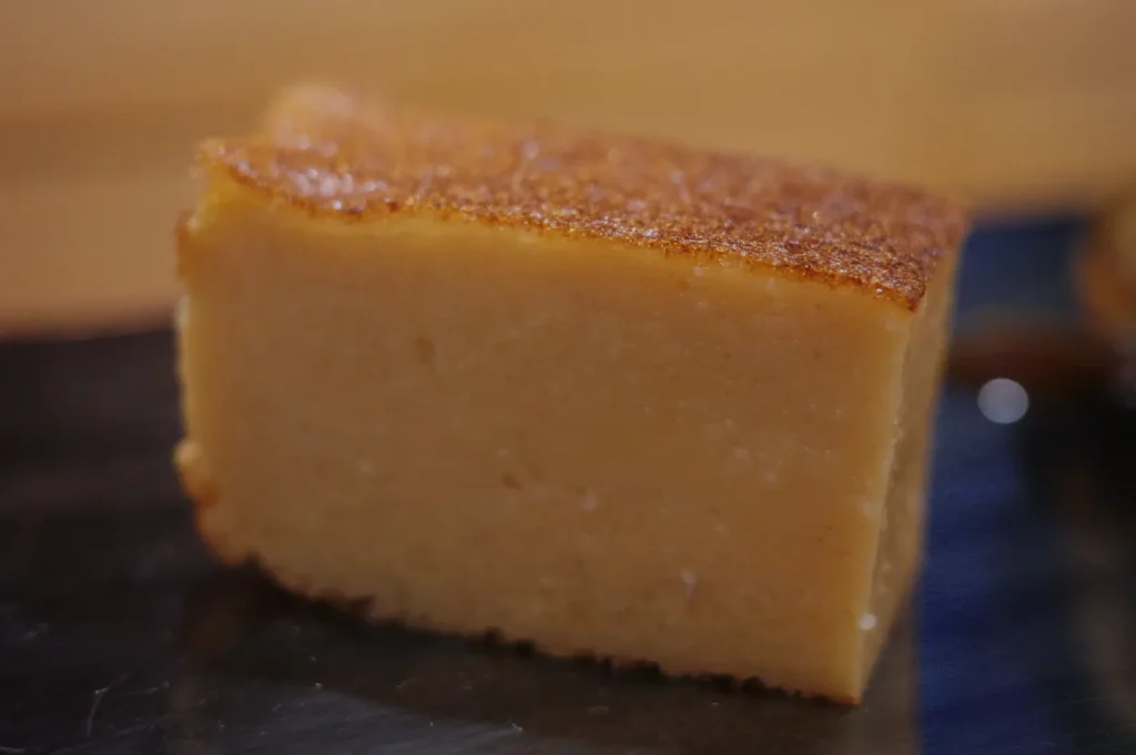 A close-up of a rectangular piece of cake with a golden-brown top and a smooth, pale yellow interior.