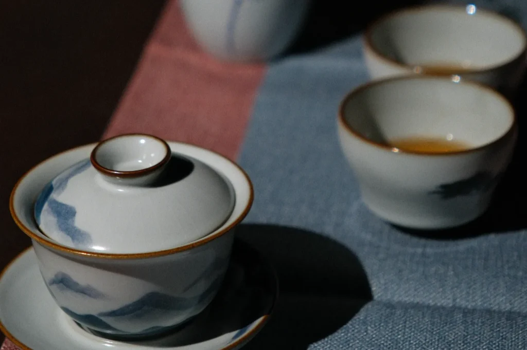 A set of ceramic tea cups and a teapot with a mountain design on a textured surface.