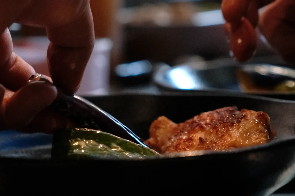 A person’s hand is using a spoon to cut or serve food that appears to be on a plate with green leaves.