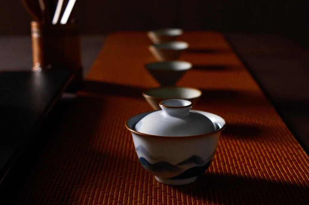 A row of traditional Chinese tea cups and a lidded gaiwan rests on a warm wooden tea tray, creating a quiet, intimate mood.