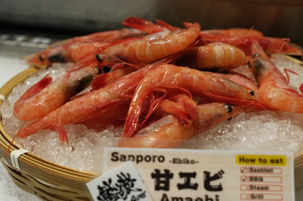 A basket of fresh amaebi (sweet shrimp) on ice, with a sign displaying how to eat them.