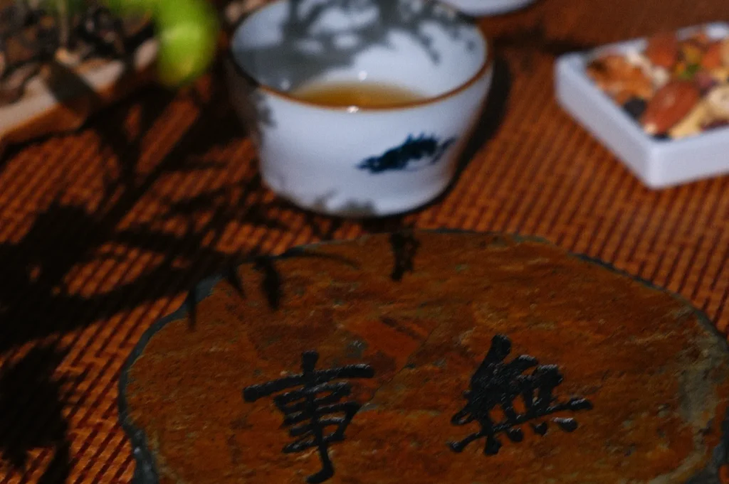 A close-up of a stone slab with Chinese characters, a tea cup, and a small plate of snacks in the background.