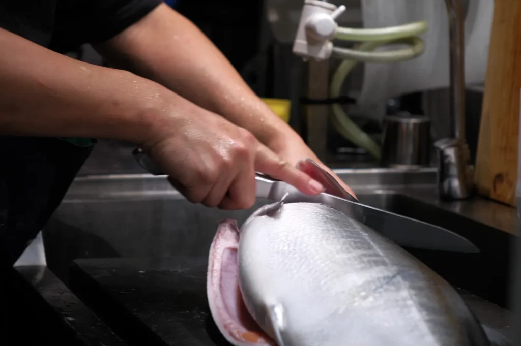 A person filleting a fish on a cutting board with a knife.