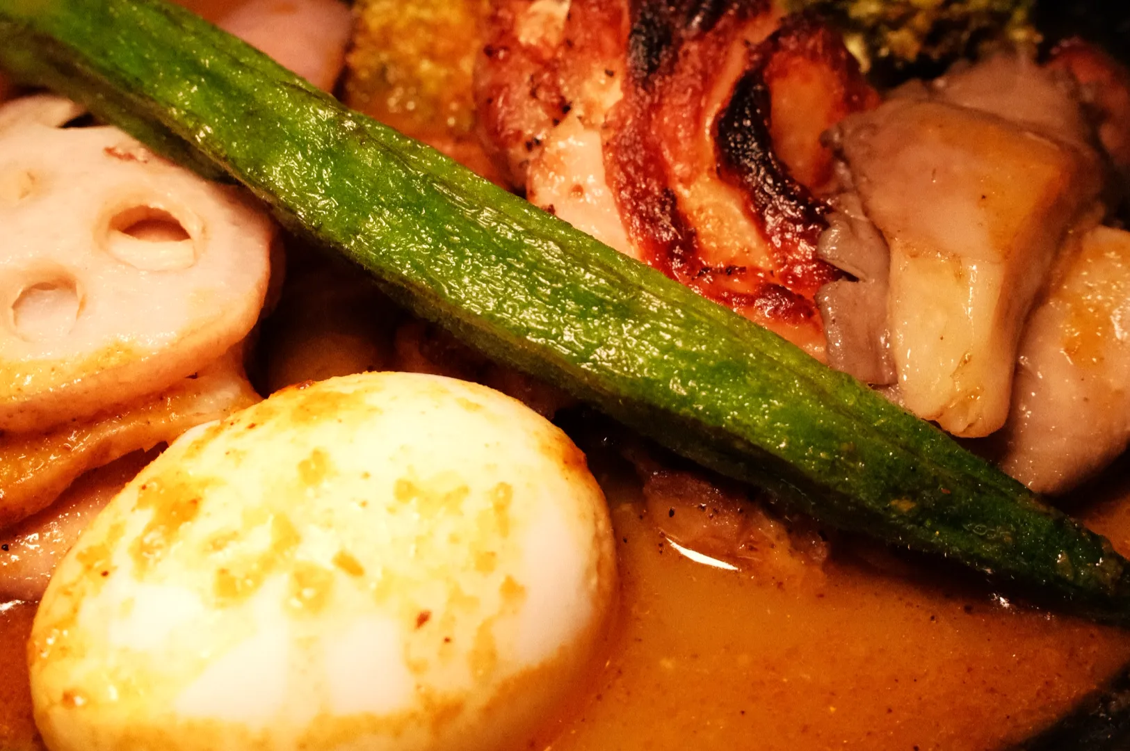 Close-up of a rich, savory dish with lotus root, a green vegetable stalk, browned mushrooms, and a golden seared round ingredient in sauce.