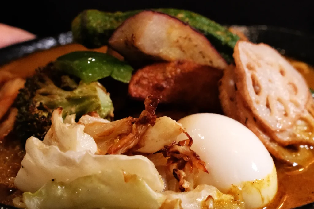 A close-up of a hearty, glossy vegetable curry with a boiled egg, cabbage, lotus root, greens, and browned vegetables, served warm and inviting.