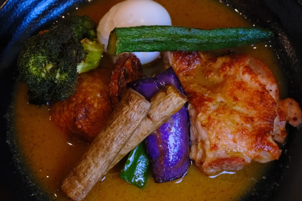 A comforting bowl of chicken curry in rich orange sauce, topped with broccoli, zucchini, eggplant, mushrooms, and a white onion.